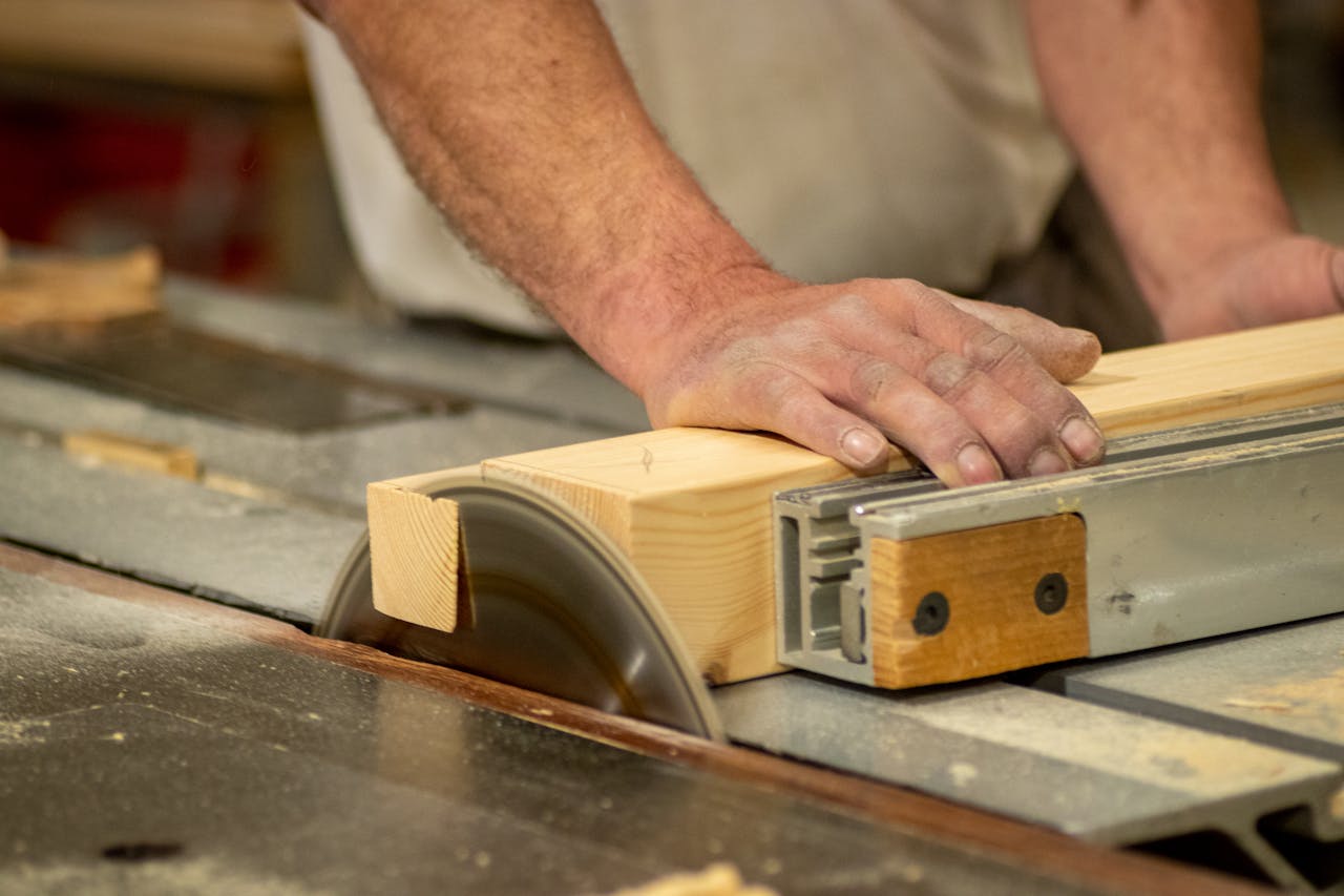 Hands of a carpenter cutting wood on a table saw, showcasing craftsmanship and precision.