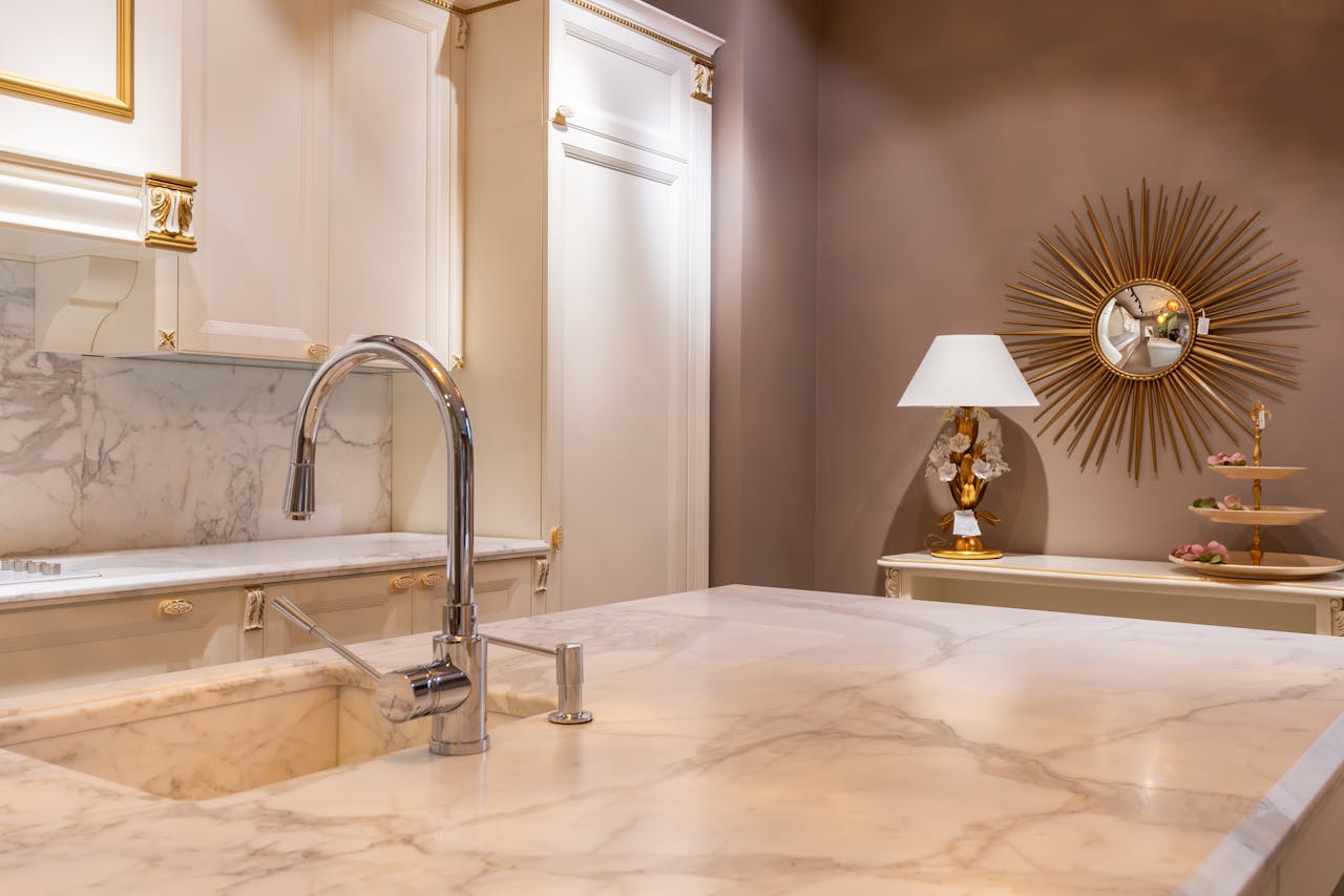 Mastering the First Impression: Your intriguing post title goes here Sink with faucet on marble counter in modern stylish kitchen with white cabinets and glowing lamp near decorations in apartment
